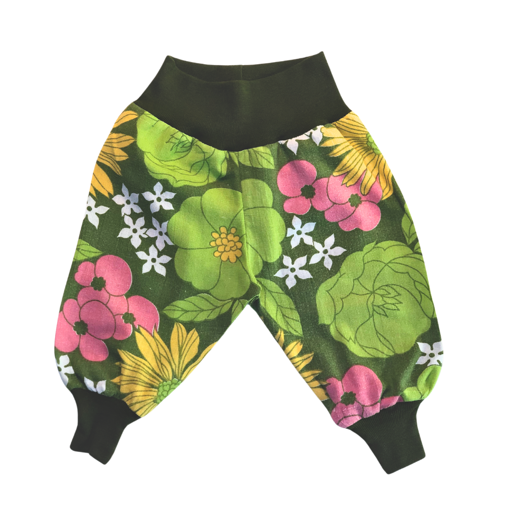 Puffiga barnbyxor i blommigt återbrukat bomullstyg med mörkgröna muddar vid midja och fötter.