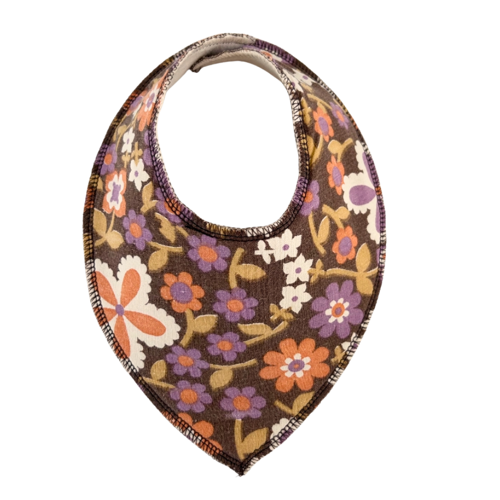 dregglis sydd i ett brunt återbrukat tyg med blommor i lila, orange, grönt och vitt.