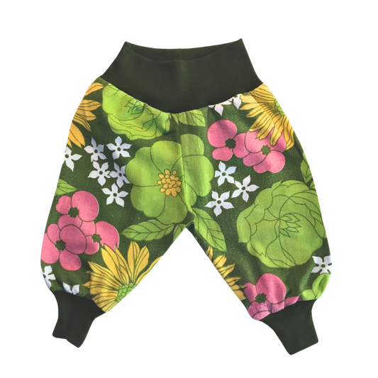 Puffiga barnbyxor i blommigt återbrukat bomullstyg med mörkgröna muddar vid midja och fötter.