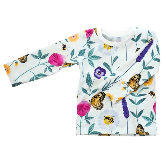 Platt liggande långärmad trikåtröja i vit ekologisk bomullsjersey med färgglatt mönster av blommor och insekter i lila, rosa, gult och turkos.